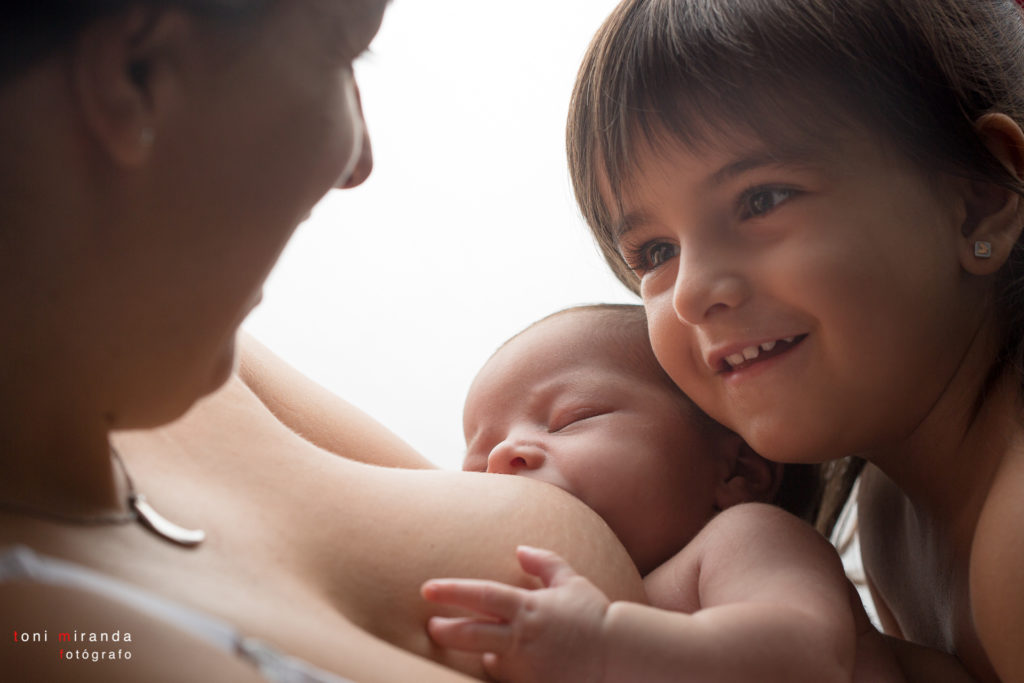 una recien nacida mamando y su hermana mirando a su madre