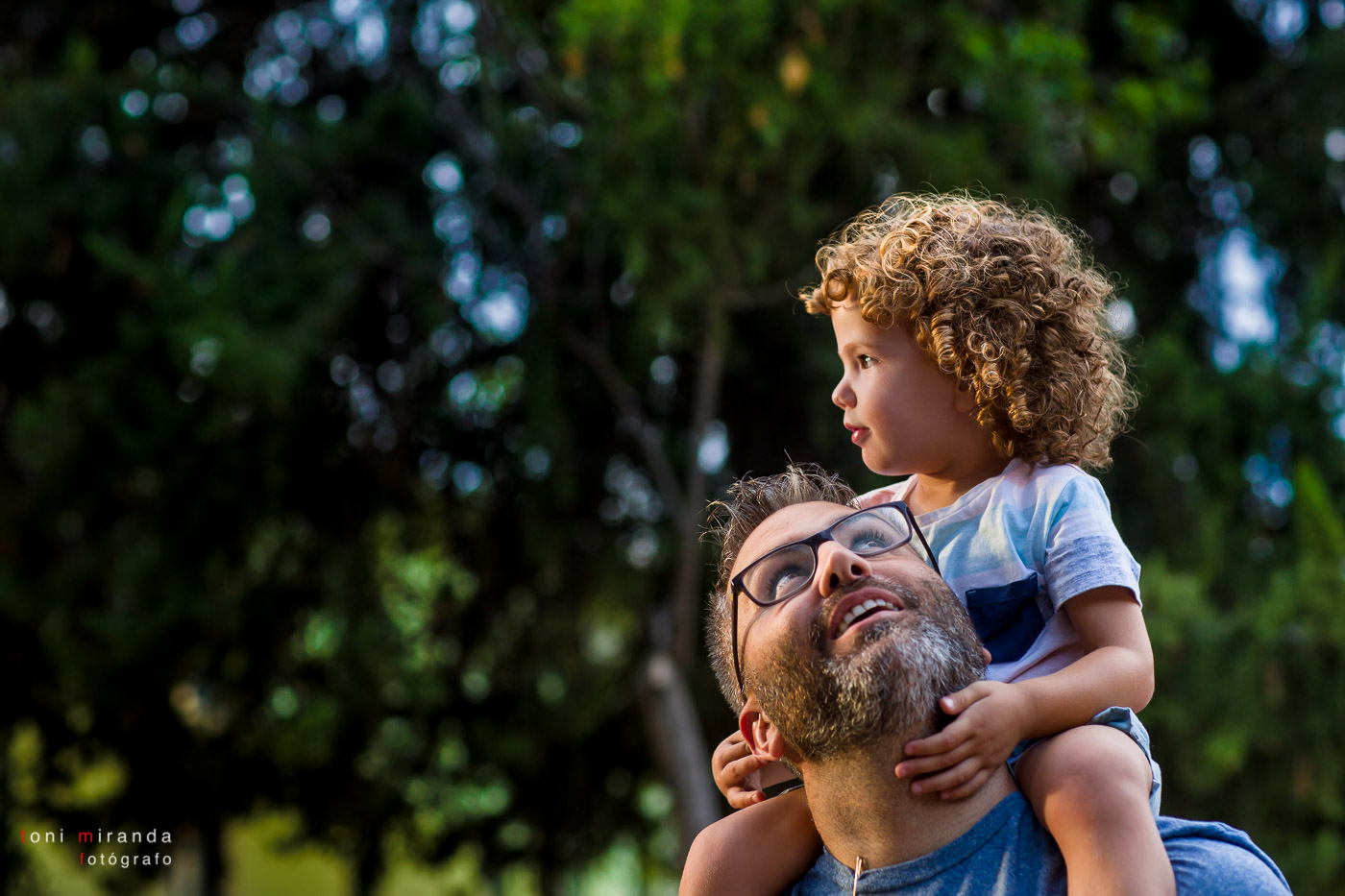 niño subido a hombros de su padre jugando en el parque
